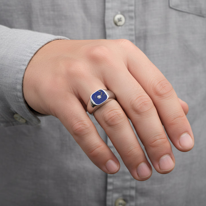 Hand wearing a ring with a navy blue stone against a gray shirt background