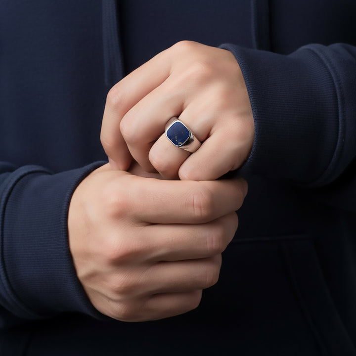 Close-up of a person's hands with a deep-blue stone ring on a dark background