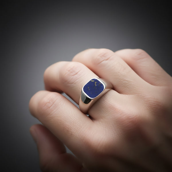 Hand wearing a signet ring on a dark background