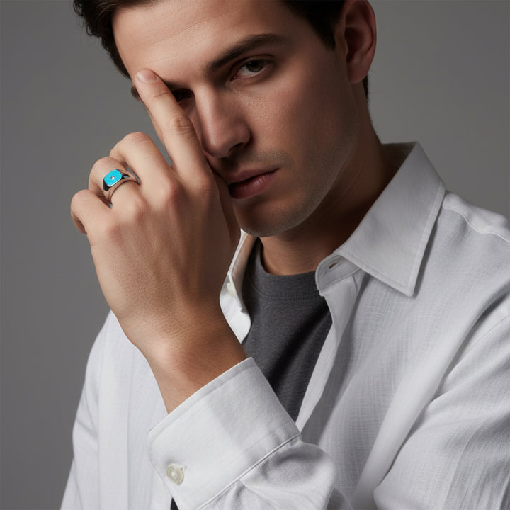 Man wearing a white shirt, posing with his hand on his face against a dark background.