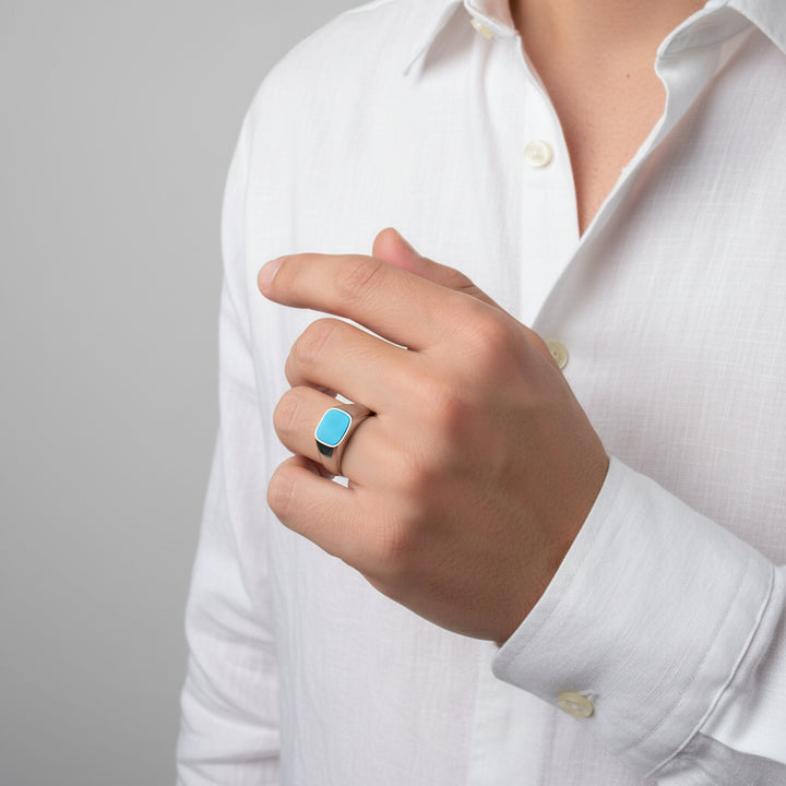 Hand wearing a blue turquoise ring with a white shirt on a gray background